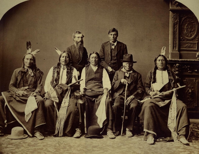 [Brule Delegation consisting of: (standing L to R) Agent Pollock or Major Andrus; Louis Roubedeaux (interpreter); (seated L to R) Black Crow; Iron Wing; Spotted Tail; Coarse Voice?; White Thunder.]
 Studio portrait of a group of adult males in native and